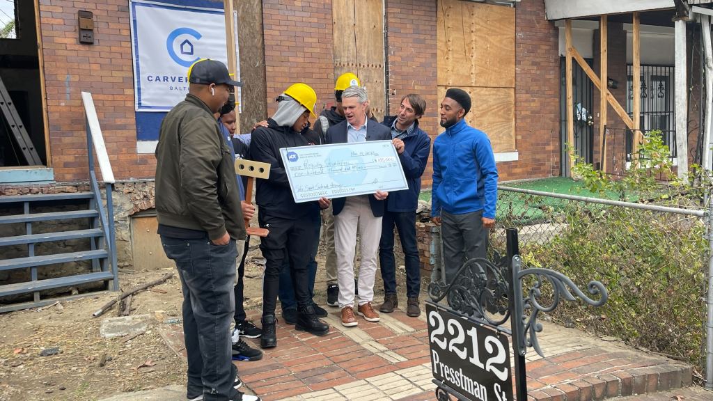 John Owens, ADT Senior Vice President, presents a $100,000 check to leaders of the Requity Foundation and participants in the Carver House rehabilitation project. Baltimore Mayor Brandon Scott is at right. An innovative partnership between ADT and Requity Foundation will provide a hands-on learning lab for students and help revitalize the community.