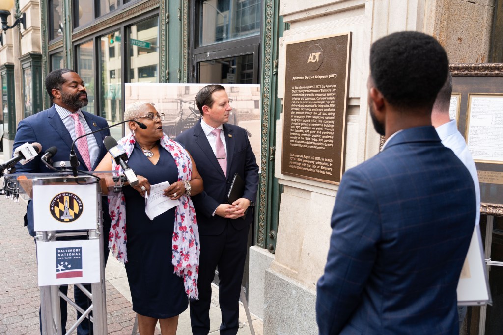 Shauntee Daniels, Baltimore National Heritage Area Executive Director, reads the historical marker on the site of ADT's founding in Baltimore on ADT's 149th anniversary, Aug. 14, 2023. Also in attendance at the unveiling were (from left) Nick Mosby, Baltimore City Council President, Bill Ferguson, Maryland State Senate President, and Brandon Scott, Baltimore Mayor.