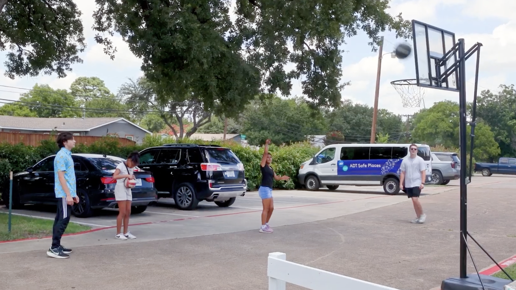 Kids shoot baskets at the All Things Made New drop-in center in Irving, Texas. ADT recently donated $100,000 to the nonprofit, along with a security system for the center and the 10-passenger van seen in the background.